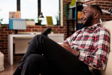Poster - African american man watching television film, having fun with comedy movie tv and working remotely laptop. Sitting on couch to work laptop, looking at show tv channel home.