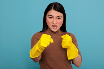 Wall Mural - Angry aggressive asian housewife in standing in fight pose at chores rubber gloves isolated on a blue background, Ready for his duty, Cleaning home concept, Female in confidence face expression