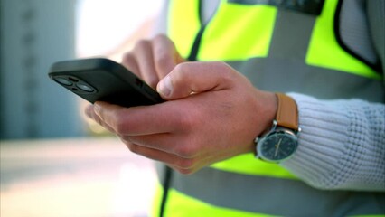 Poster - Construction worker texting on a phone, standing outdoors at a building site. Closeup of an architect or engineer checking a design development or online model, communication for design approval