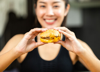 Wall Mural - Beautiful female in sportswear hamburger junk food high calorie food and health risks. Hungry young woman eating unhealthy food