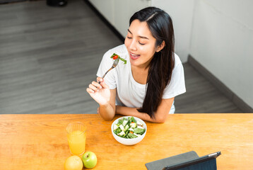 Wall Mural - Young female eating organic greens vegetable salad in weight loss diet and wellness on table. Beautiful woman happily eat a healthy salad breakfast in kitchen in the morning. Diet food concept.