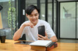 © bongkarn - Happy asian guy sits at his working desk, using his smartphone to chat with his friends
