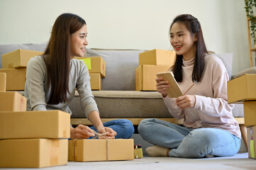 Two young Asian female small online business shop owners helping pack shipping orders