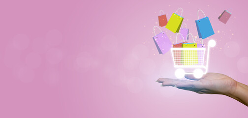 Female hand holding a small shopping cart with colorful shopping paper bags isolated on pink background.