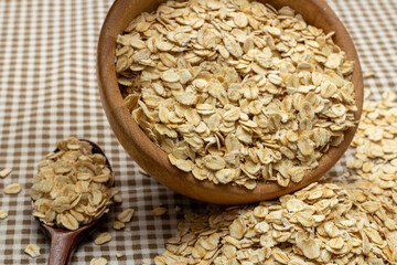 Wall Mural - Concept of healthy food, Oat flakes in wooden bowl and fall on gingham cloth background