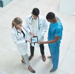 Poster - Group of doctors working on digital tablet while standing in the hospital hallway and talking. Top view of healthcare employees analyzing test results and treatment in medicare clinic with technology