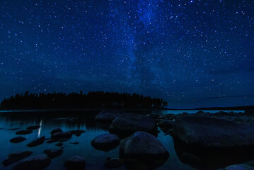 Wall Mural - Astrophotography of landscape with a beautiful night starry sky and Milky way over water of sea with stones