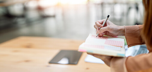 Closeup of woman's hand writing note on schedule book, business banner background.