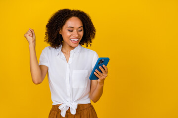Wall Mural - Photo of delighted excited girl raise fist luck achievement hold telephone isolated on yellow color background