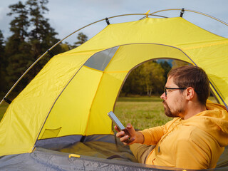 Wall Mural - trip to Caucasus mountains, Arkhyz, Teberdinsky reserve. Man traveler relaxing in mountains in tent camping outdoor , uses app on smartphone. Travel adventure lifestyle concept hiking active vacations