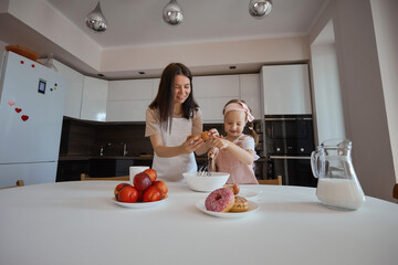 Wall Mural - A happy loving family is preparing a bakery together. Mother and daughter cook pancakes and have fun in the kitchen. Homemade food and a little helper. pour milk