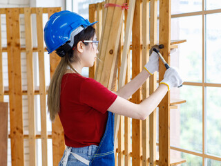 Wall Mural - Asian professional female engineer architect foreman labor worker wears safety goggles hard helmet jeans apron and gloves using pencil writing note on paper clipboard on table with working equipment