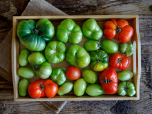 Top View Of A Wooden Box With Farm Tomatoes Of Different Varieties And Different Colors. Freshly Picked Tomatoes. Against The Backdrop Of A Rustic Farm Floor. Flat Lay.