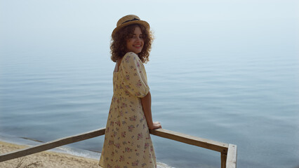 Wall Mural - Playful girl looking camera with seductive smile standing in front calm ocean. 