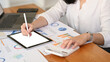© Prathankarnpap - Professional businesswoman analyzing stock charts, using digital tablet on wooden office desk