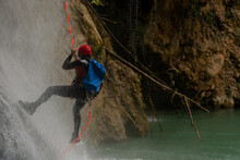 Unrecognizable Man With Helmet, Neoprene Dress And Harness Practicing Rappelling In A Waterfall