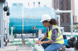© amorn - Female engineer working with laptop computer for maintenance in sewer pipes area at construction site. African American woman engineer working in workplace at rooftop of building