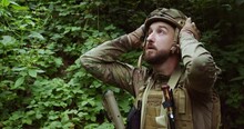 A Tired Bearded NATO Soldier Takes Off His Helmet Looks Up At The Sky Then Straightens His Hair And Looks At The Camera. Medium Plan. Ukrainian Soldier In Ammunition