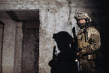 Fototapeta  - Portrait of a Ukrainian defender in the dugout. A soldier with a weapon in his hands casts a shadow on the wall.