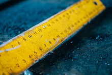 Yellow Metal Ruler With Scale Rests On Dirty Metal Workbench. Close-up Measuring Tape Measure. Abstract Background.