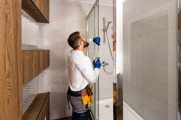 The worker is connecting the glass walls of the shower enclosure with a metal bar.