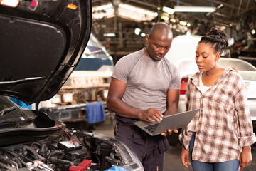 African american  Two mechanics - man examining car engine. Auto mechanic working in garage.Car Mechanic Detailed Vehicle Inspection. Auto Service Center Theme.