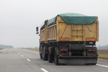 Wall Mural - Heavy loaded yellow dump truck with tented trailer on the country highway road