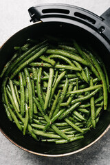 Seasoned raw green beans in an air fryer basket