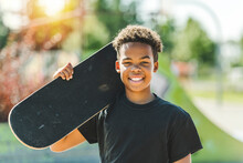 Afro-American Boy With Black T-shirt Posing With His Skateboard With The Sky In The Background