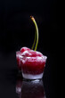Cherry in ice glass against black background