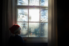 Boy In Santa Hat Looking Through Window While Standing At Home