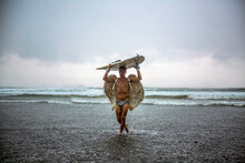 Man Wearing Angel Wings Carrying Surfboard While Walking In Sea Against Cloudy Sky