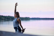 A woman is practicing yoga and balancing on one foot on the dock near the river in nature.