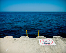 No Swimming Sign On Pier Over Sea Against Clear Blue Sky
