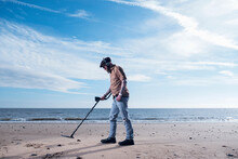 Side View Of Man Using Recreational Metal Detector At Horsey Beach Against Sky