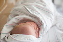 Close-up Of Newborn Baby Sleeping While Being Wrapped In Blanket