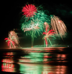 Multi coloured fireworks exploding over an ocean in the night sky.