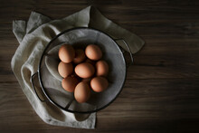 Overhead View Of Brown Eggs In Colander With Napkin On Wooden Table
