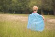© Cavan Images - Rear view of boy wearing blue cape while playing on grassy field at public park