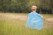 Rear View Of Boy Wearing Blue Cape While Playing On Grassy Field At Public Park