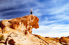 Low Angle View Of Carefree Man Standing On Rock Formation Against Cloudy Sky At Desert