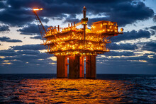 Illuminated Oil Exploration Platform In Sea Against Cloudy Sky During Sunset