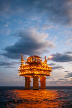 Illuminated Oil Exploration Platform In Sea Against Cloudy Sky