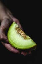 Cropped Hand Of Woman Holding Cantaloupe Slice Against Black Background