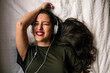 © Cavan Images - Overhead view of cheerful teenage girl listening music while lying on bed at home