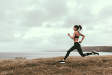 Woman Running On Grassy Field By Sea Against Cloudy Sky