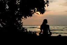 Rear View Of Silhouette Woman Sitting At Beach Against Sky During Sunset