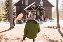 Rear View Of Girl Sitting On Swing At Playground During Winter