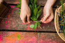 Cropped Hands Of Woman Tying Herbs With String Over Painted Wooden Table