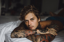 Portrait Of Shirtless Tattooed Man Lying On Bed At Home